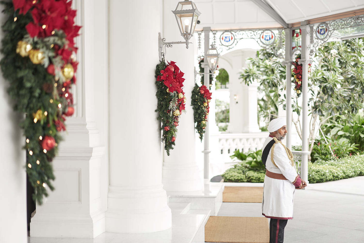 Doorman in uniform standing at the entrance driveway of Raffles Hotel Singapore, with classic architecture in the background.