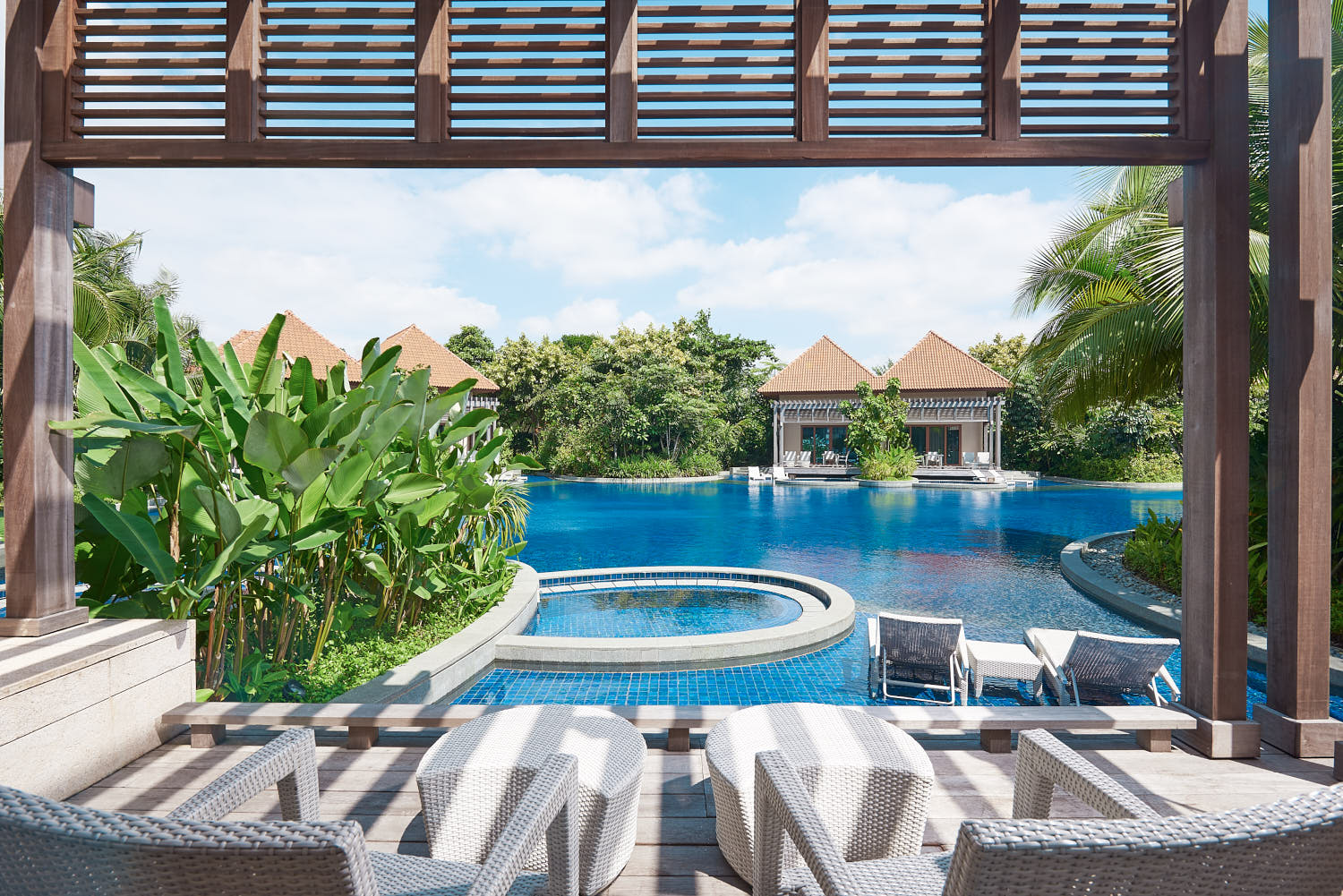 Tropical resort pool at Equarius Villas at RWS, featuring a spacious deck, lush greenery, and tranquil surroundings.