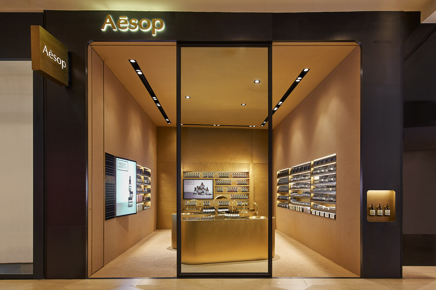 Aesop retail interior with high ceilings and warm brass-colored finishes.