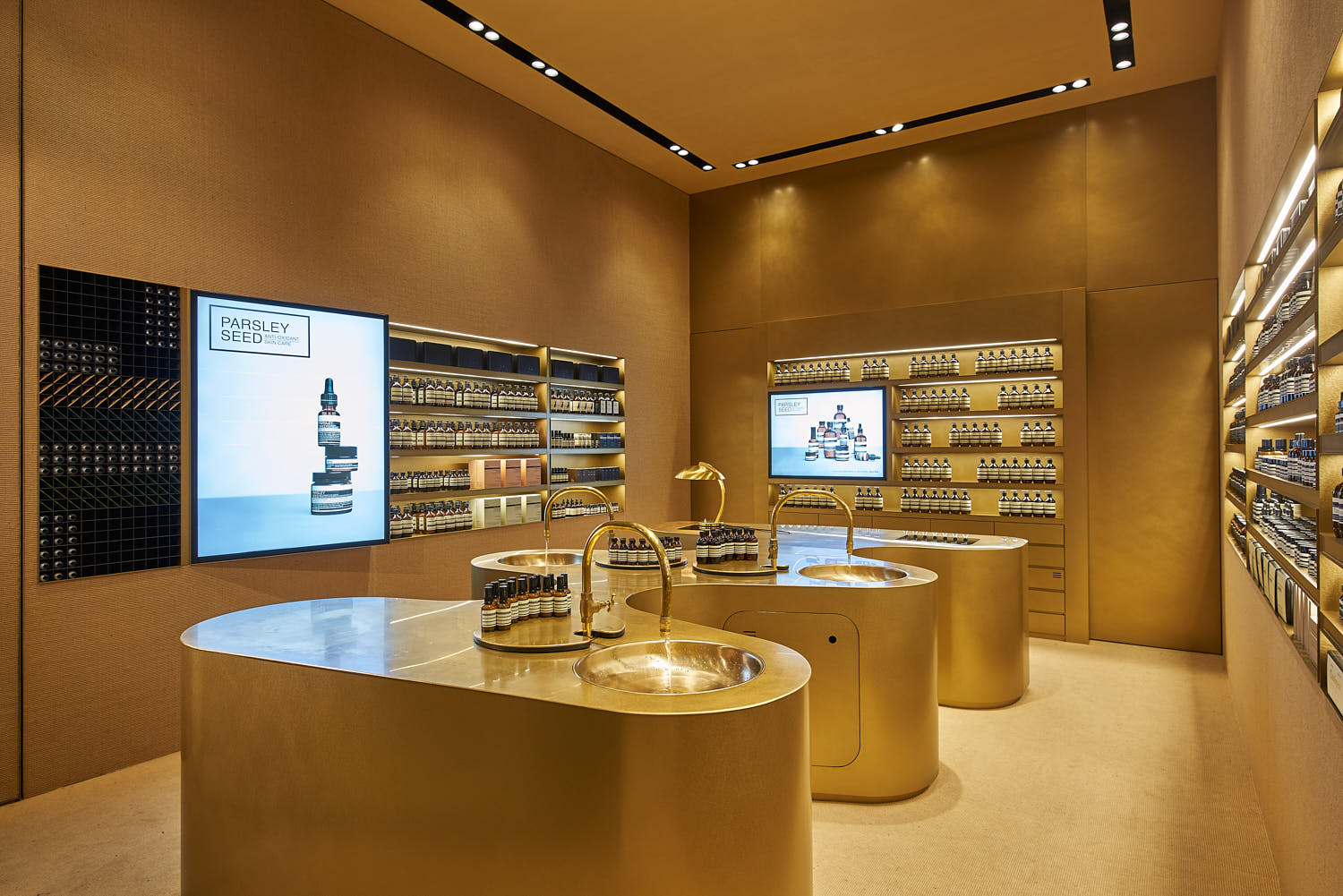 Brass-toned sink installation with brushed metal taps inside Aesop store.