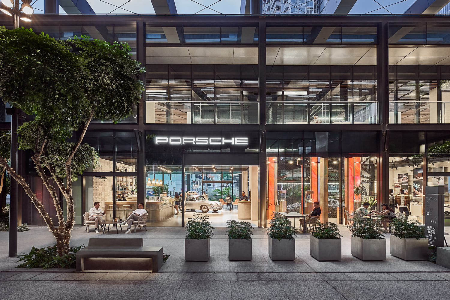 Flagship Porsche showroom at dusk with expansive glass façade and lit interiors.