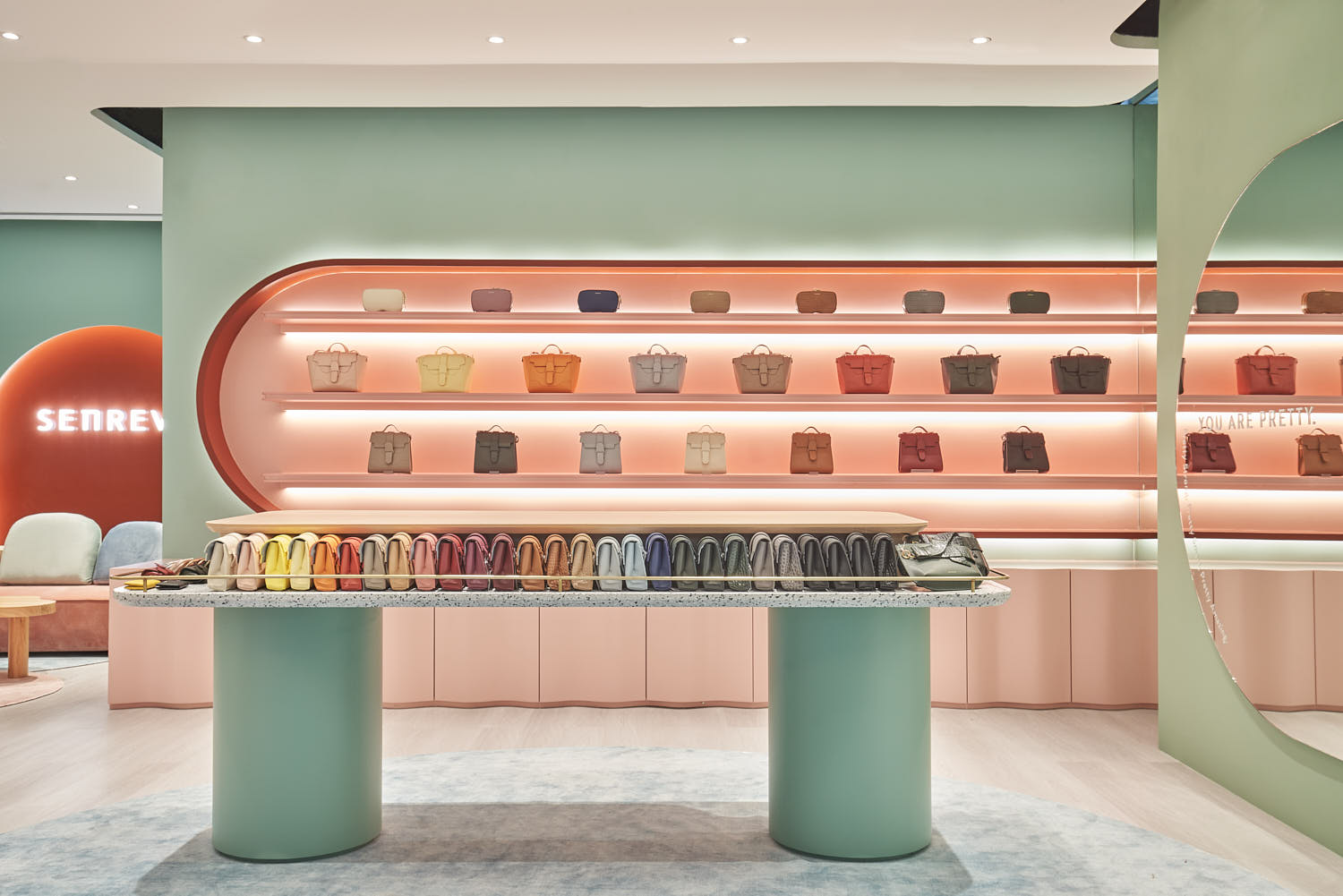 Senreve store interior featuring pastel-colored walls with handbags and purses displayed on shelves and tabletops.